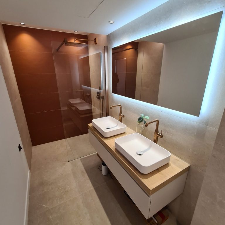 Salle de bain avec douche et deux vasques à poser sous un miroir éclairé